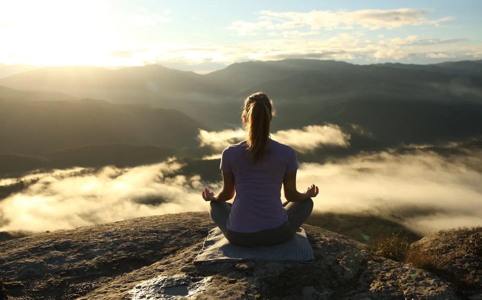 A woman meditating on a rock above the clouds at sunrise