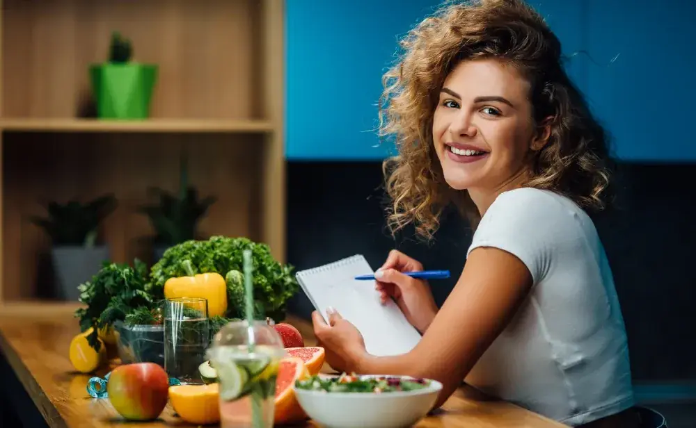 A health coach making notes at a table of fresh fruit, vegetables and juice