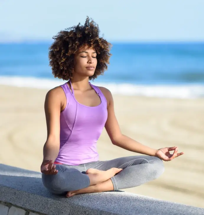 A woman meditating cross-legged on a beach